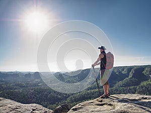 Hiker with red backpack on cliff hold trekking sticks