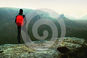 Hiker with red backpack on sharp sandstone rock in rock empires park and watching over the misty and foggy spring valley