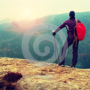 Hiker with red backpack on sharp sandstone rock in rock empires park and watching over the misty and foggy spring valley