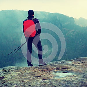 Hiker with red backpack on sharp sandstone rock in rock empires park and watching over the misty and foggy spring valley