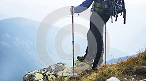 Hiker on a rock on top of mountain with trekking sticks and back