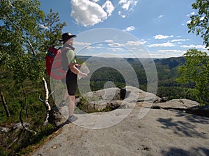 Hiker in shorts wear cowboy hat and red back pack, stay on rock