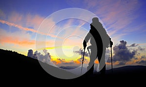 Hiker silhouette on mountain peak looking at sunset