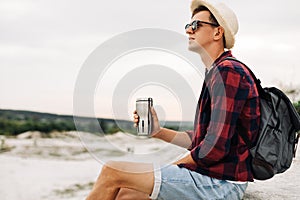 Hiker sits on the top of the mountain, man with a cup of coffee sits on a rock with a view of the nature around