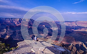 Hiker sitting at edge of rock outcrop with panoramic view of the Grand Canyon