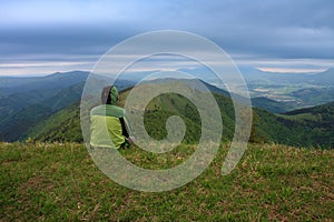 Hiker sitting in grass , on background mountain Osnica , Mala Fatra, Slovakia in spring cloudy morning