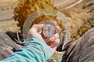 Hiker sitting on a high rock holds a compass in front of her feet in trekking boots and a high cliff with an asphalt