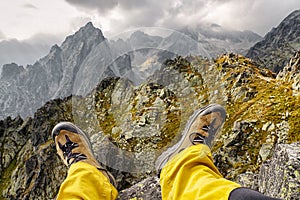 Hiker sitting on the hill and looking on mountains. Hiking boots on legs of tourist