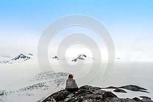 Hiker sitting at the summit of a mountain overlooking the Harding Ice Field in Alaska enjoying the spectacular and surreal view