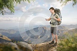 Hiker with a smartphone standing in front of a tropical mountain panorama