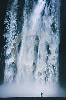 Hiker standing in front of gigantic Skogafoss waterfall in Iceland