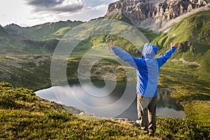 Hiker standing with raised hands near the beautiful mountain lake and enjoying view