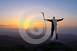 Hiker standing on top of a mountain with raised hands and enjoying sunrise