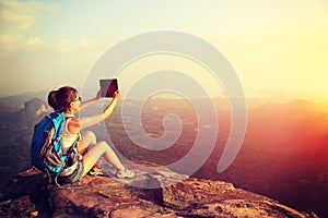 Hiker use digital tablet taking photo at mountain peak cliff