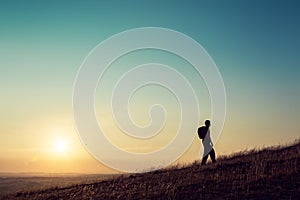 A hiker walking up hill, silhouetted against the setting sun