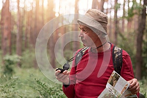 Hiker wearing red casual sweater and cap, posing with backpack, searching right direction with compass, being lost in forest, lit