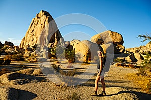 Hiker woman climbing the rocks in a beautiful warm sunset light in the Joshua Tree National Park, California, USA