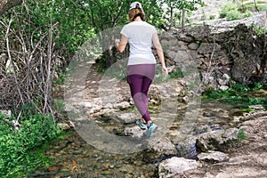 Hiker woman crossing a river jumping over stones