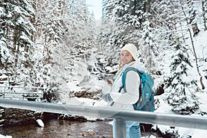 Hiker woman in front of small waterfall in the woods during winter