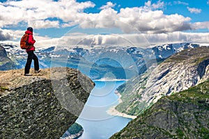 Hiker woman stands at rock and looks at aerial view in the mountains.  Amazing nature view on the way to Trolltunga. Location: