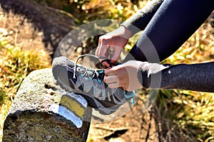 Hiker woman tying her trekking shoes on a hiking stone marking the tourist route