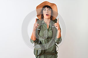 Hiker woman wearing backpack hat and water canteen over isolated white background amazed and surprised looking up and pointing
