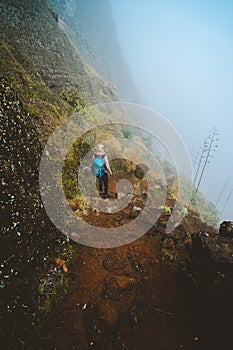 Hiker women with backpack walking down the trekking path. The steep arid slope of the rock. The fog encase the mountain
