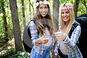Hiker women friends with backpack walking on path in summer forest