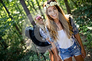 Hiker women friends with backpack walking on path in summer forest