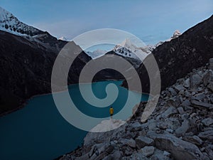 Hiker in yellow jacket at blue turquoise alpine mountain lake Laguna Paron in Caraz Huaraz Ancash Cordillera Blanca Peru