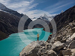 Hiker in yellow jacket at blue turquoise alpine mountain lake Laguna Paron in Caraz Huaraz Ancash Cordillera Blanca Peru