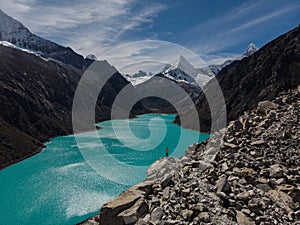 Hiker in yellow jacket at blue turquoise alpine mountain lake Laguna Paron in Caraz Huaraz Ancash Cordillera Blanca Peru