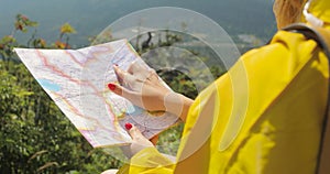 Hiker in a yellow raincoat looking at map from mountain top. woman with map in mountains 4k
