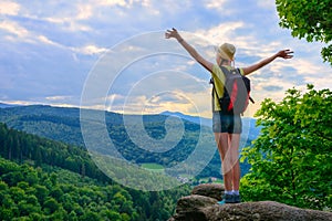 Hiker young girl standing with hands up achieving the top, admiring mountain landscape.