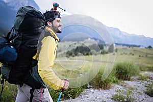 Hiker young man with backpack and trekking poles looking at the mountains in outdoor