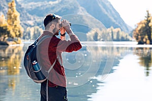 Hiker young man traveler with backpack looking the landscape with binoculars in the lake