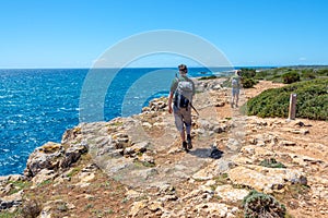 Hikers on a coastal path by the sea in Menorca, Balearic islands Spain