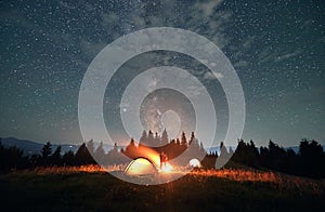 Hikers standing near campfire under beautiful starry sky.