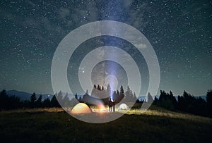 Hikers standing near campfire under beautiful starry sky.