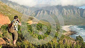 Hikers stands with raised arms on mountain top against mountains