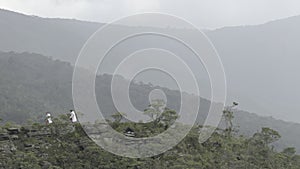 Hikers with White Raincoats Walking on Misty Mountain Ridge