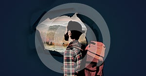 Hiking adventurer man looking through surreal paper hole at nature landscape