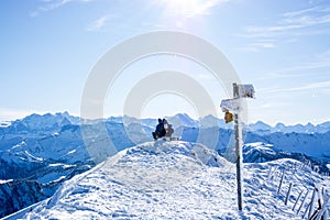 hiking couple at the summit of the snowy mountain sitting on the bench, enjoying the panorama of the swiss alps. success and