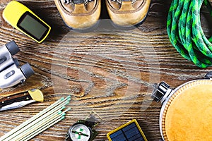 Hiking equipment with boots, compass, binoculars, matches, travel bag on wooden background. Active lifestyle concept.