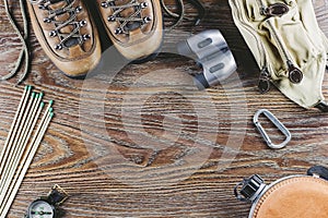 Hiking equipment with boots, compass, binoculars, matches, travel bag on wooden background. Active lifestyle concept.