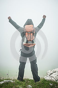 Hiking man with backpack open arms on foggy mountain peak