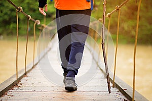 Hiking man crossing river in walking in balance on hinged bridge in nature landscape. Closeup of male hiker trekking