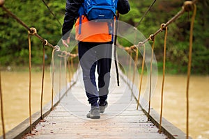 Hiking man crossing river in walking in balance on hinged bridge in nature landscape. Closeup of male hiker trekking