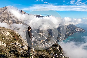 Hiking man with scenic view from Monte Comune on clouds covering the coastal town Positano at the Amalfi Coast, Campania, Italy.