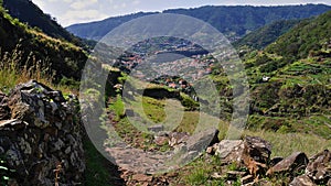 Hiking path besides rock wall in valley with view over Machico town in the east of Madeira, Portugal.